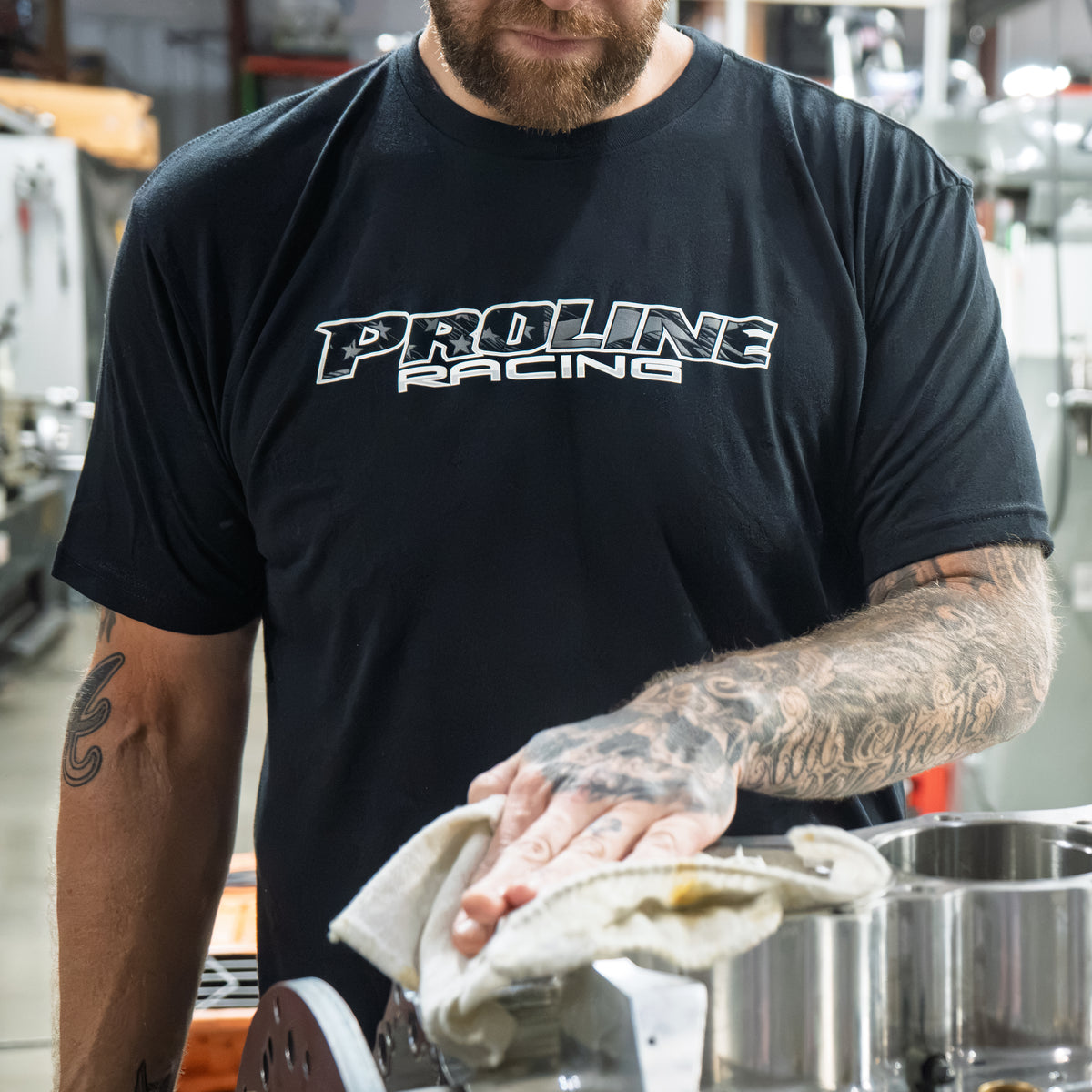 Person wearing a Proline Racing shirt cleaning a metal part in a workshop.