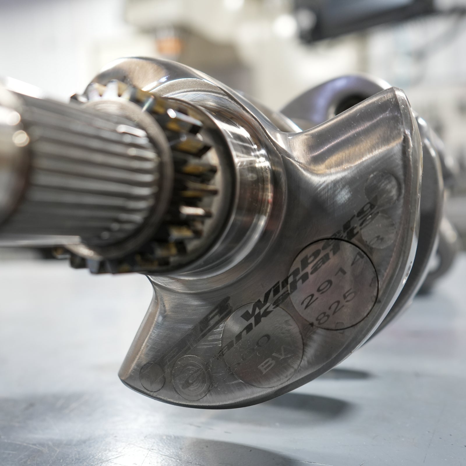 Metal crankshaft on a table with machinery in the background