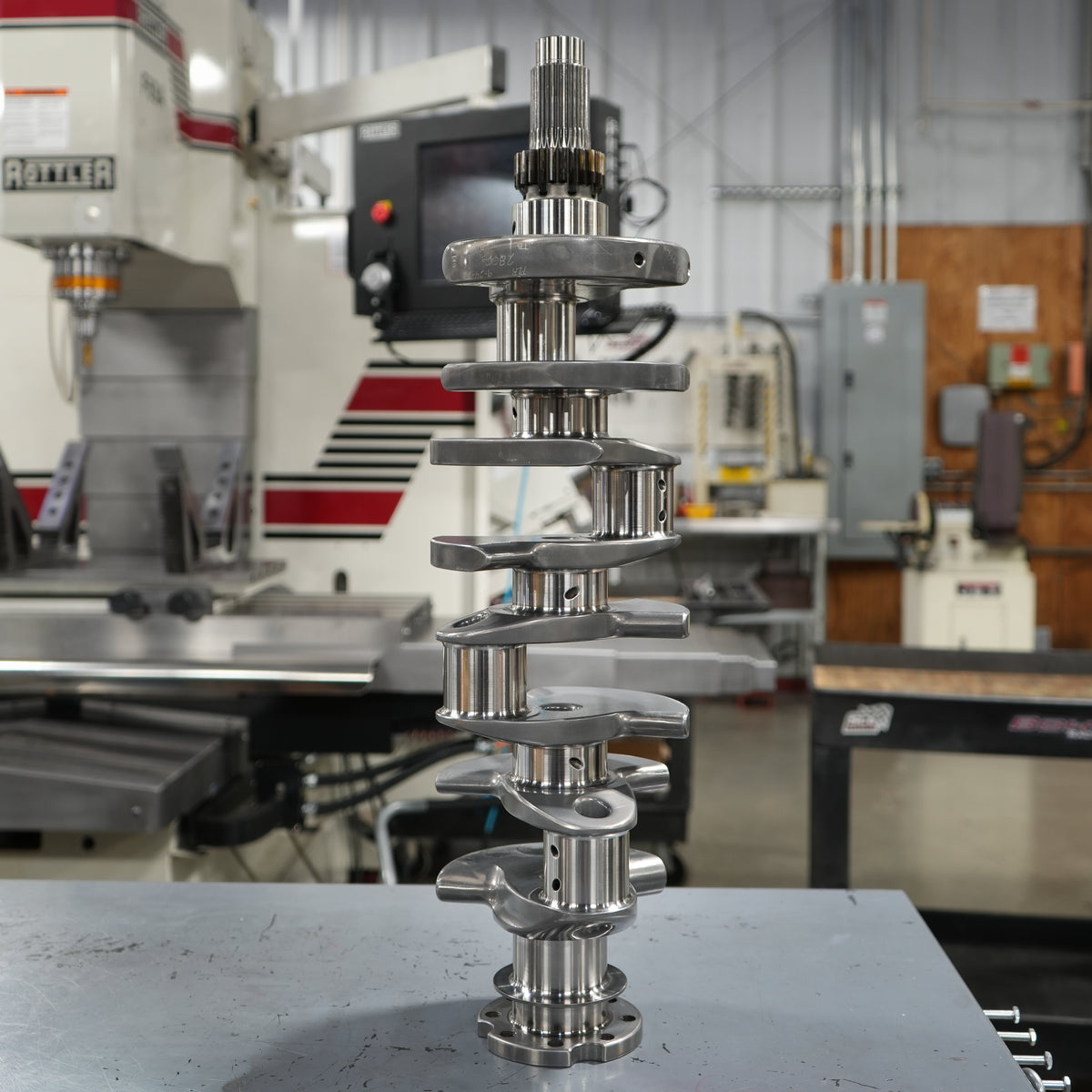 Metal crankshaft on a table with machinery in the background